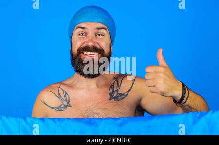 L'uomo felice in testa di cappuccio della doccia mostra il pollice in su. Tempo di bagno. Doccia e lavaggio. Buon umore. Foto Stock