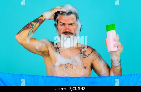 Uomo in barbuto in doccia con bottiglia di shampoo. Bel ragazzo con schiuma sulla testa lavando i capelli. Cura dei capelli. Foto Stock