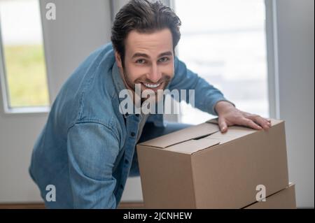 Uomo che si piega sopra le scatole sorridendo alla macchina fotografica all'interno Foto Stock