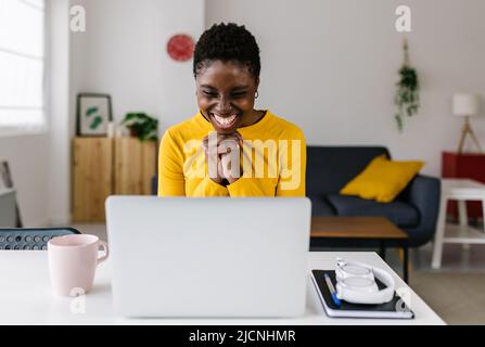 Giovane donna africana eccitata che festeggia il successo guardando lo schermo del laptop Foto Stock