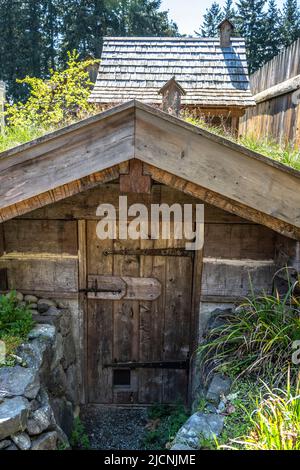 Edificio adibito a deposito di patate durante l'estate con la casa fumaria sullo sfondo presso il Fort Nisqually Living Museum di Tacoma, W. Foto Stock