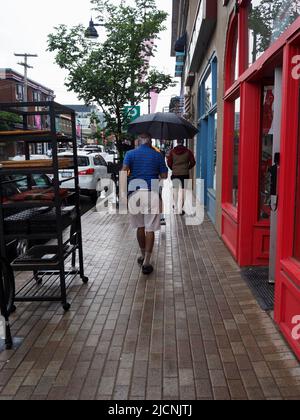 Vecchio uomo in pantaloncini e un ombrello che cammina lungo la strada su una Domenica piovosa a Ottawa, Ontario, Canada. Foto Stock