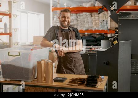 Sorridente il proprietario della fabbrica di torrefazione del caffè sul suo posto di lavoro guardando la macchina fotografica Foto Stock