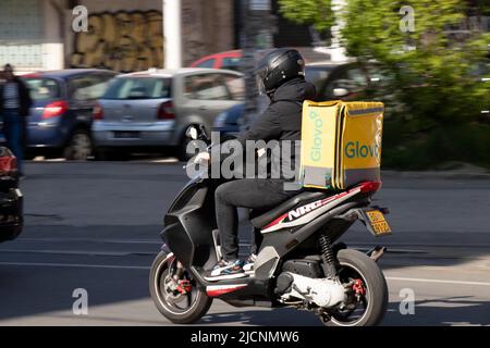 Belgrado, Serbia - Aprile, 15, 2022: Corriere che lavora per il servizio di consegna di cibo Glovo in sella a uno scooter con container sulla schiena, sulla strada della città Foto Stock