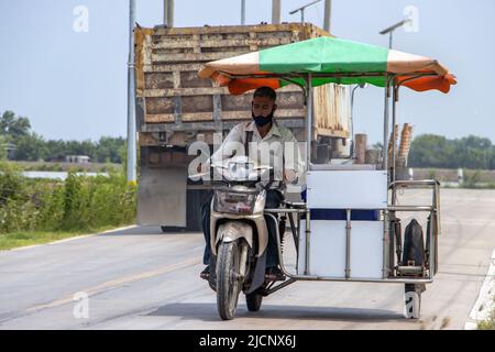 SAMUT PRAKAN, THAILANDIA, 01 2022 GIUGNO, un distributore di gelati percorre una moto a tre ruote lungo una strada del villaggio Foto Stock