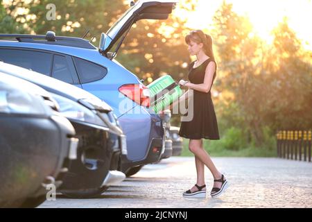 Giovane donna conducente che mette valigia valigia borsa all'interno della sua auto. Concetto di viaggio e vacanza Foto Stock