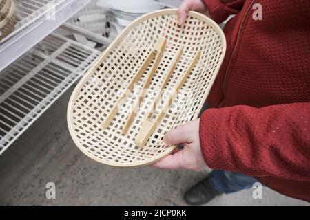 La ragazza caucasica acquista in un negozio piatti di pane in vimini di legno con tenaglie di legno Foto Stock