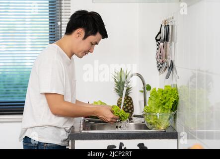 giovane uomo che lavano le verdure nel lavandino in cucina a casa Foto Stock