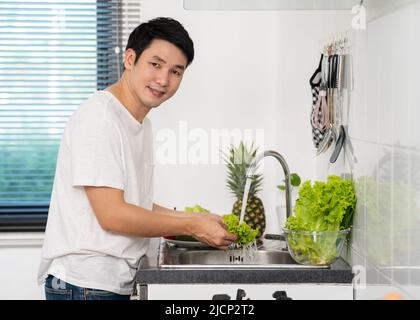 felice uomo giovane lavando le verdure nel lavandino in cucina a casa Foto Stock