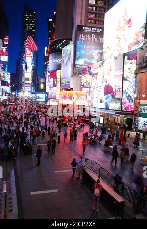 I cartelli pubblicitari illuminano la folla di persone che camminano attraverso un'affollata Times Square a New York City di notte Foto Stock