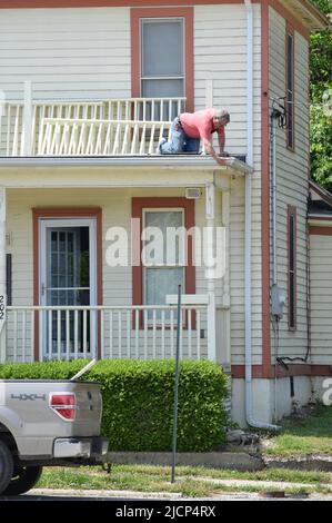 Un uomo che si inginocchiava e lavorava su un tetto di una casa Foto Stock