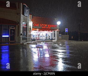 Le luci si riflettono sul parcheggio bagnato del negozio di birra e vino One Stop Market in una notte di pioggia a Irving, Texas Foto Stock