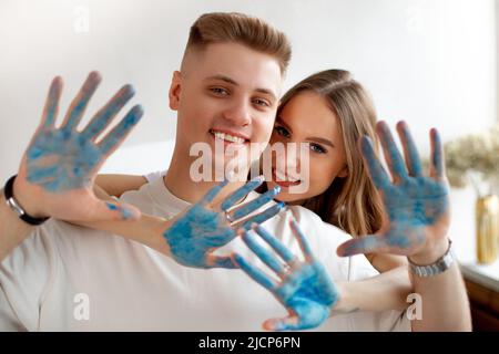 Coppia giovane che si unisce. Donna e uomo che guardano la macchina fotografica e mostrano palme dipinte blu. Foto Stock