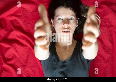 La ragazza si trova in un letto su un foglio rosso e allunga le braccia fino alla cima, dormire e riposare a casa a letto, comfort e intimità Foto Stock