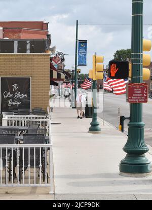 Uomo più anziano che cammina il suo cane oltre le bandiere americane che adornano Main Street nel centro storico di Grapevine, Texas, il fine settimana del Memorial Day Foto Stock