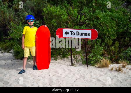 Il ragazzino è pronto per il sandboarding dalle dune di sabbia mentre si posa accanto al cartello, Kangaroo Island, South Australia Foto Stock