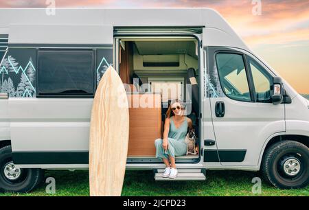 Donna seduta con il suo cane alla porta del suo camper durante un viaggio Foto Stock