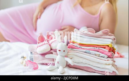 Una donna incinta sta piegando le cose del bambino. Messa a fuoco selettiva. Foto Stock