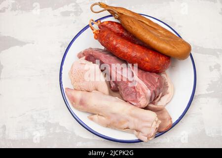 carne cruda, orecchie di maiale e salsicce affumicate su piatto bianco Foto Stock