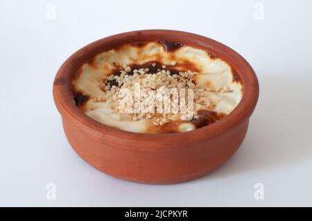 Vista del profilo di gustoso budino di riso al forno con nocciole su, dessert tradizionale noto come in turco 'Sutlaca' in casseruola di terracotta, bianco isolato Foto Stock