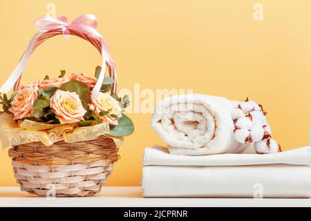 Lenzuola bianche, lenzuola e un rotolo di asciugamani. Cestino con fiori sul tavolo. Foto Stock