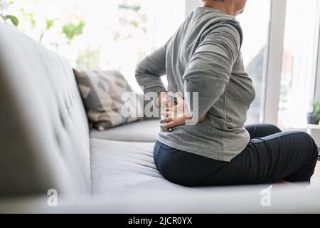 Donna anziana a casa con mal di schiena più basso Foto Stock