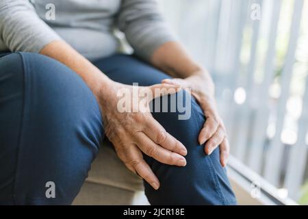 Donna anziana seduta su panca, tenendo il ginocchio doloroso Foto Stock