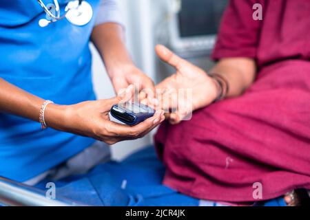 Primo piano del medico di controllo del livello di zucchero o diabete della donna malata sul letto d'ospedale - concetto di monitoraggio della salute e della cura Foto Stock