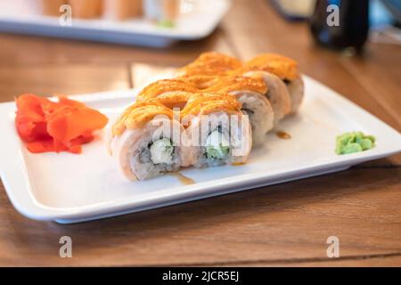 Sushi Maki al forno, panini al forno 'Philadelphia' su piatto rettangolare bianco. Salmone, riso, formaggio cremoso, cetriolo, nori alghe, salse piccanti e unagi. Foto Stock