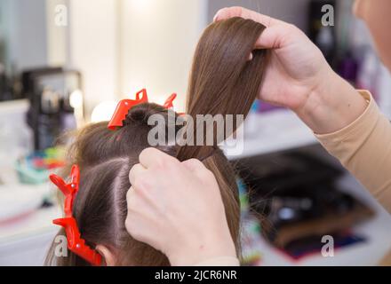 Primo piano della mano del maestro che fa un anello di capelli sulla testa di una donna. Il parrucchiere crea un'acconciatura per una giovane donna. Barbiere, concetto di business. Salone di bellezza, cura dei capelli. Foto Stock