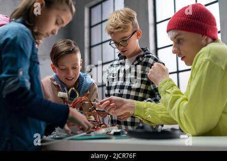 Ragazzi con insegnante che lavorano insieme al progetto con giocattoli elettrici e robot in classe robotica Foto Stock