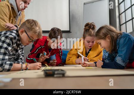 Ragazzi con insegnante che lavorano insieme al progetto con giocattoli elettrici e robot in classe robotica Foto Stock