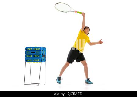 Ritratto dinamico di teen, ragazzo sportivo giocando a tennis isolato su sfondo bianco studio. Concetto di sport, realizzazioni, hobby, abilità Foto Stock