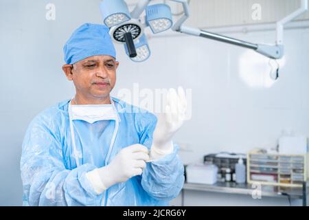 Guanti da ordito chirurgo per l'esecuzione di interventi chirurgici in sala operatoria - concetto di preparazione, fiducia e trattamento sanitario profesionale Foto Stock