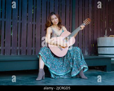 Una bella donna seduta felicemente suonando la chitarra Foto Stock