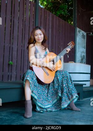 Una bella donna seduta felicemente suonando la chitarra Foto Stock