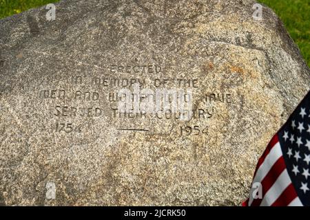 Bandiera americana e pietra 'eretto in memoria degli uomini e delle donne che hanno servito il loro paese 1754 a 1954' su un villaggio verde del New England Foto Stock