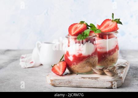 Cheesecake alla fragola. Cheesecake o trifle con fragola in vetro su sfondo vecchio tavolo grigio cemento. Cheesecake senza cottura. Dess Foto Stock