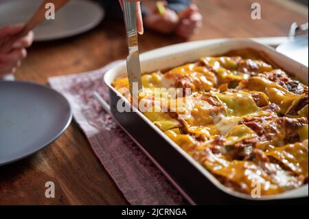 Taglio di deliziose lasagne vegane fatte in casa in una padella su un tavolo da pranzo domestico. Foto Stock