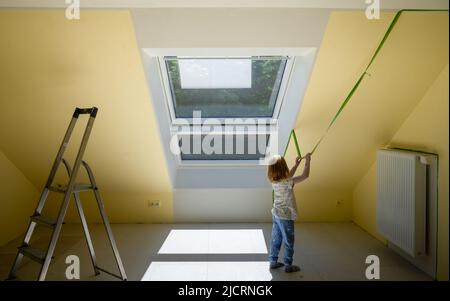 Il bambino toglie il nastro di mascheratura e crea un bordo affilato tra una parte dipinta di giallo e bianco di una parete. Foto Stock