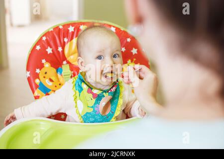 la madre nutre il bambino divertente da un cucchiaio. il bambino mangia in un seggiolone Foto Stock