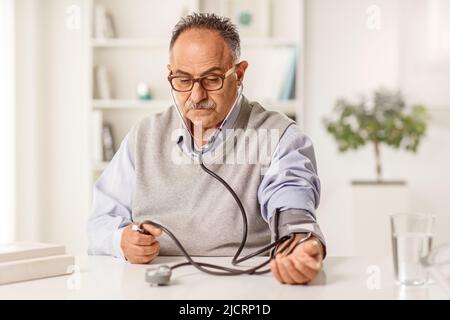 Uomo maturo che misura la pressione sanguigna a casa Foto Stock