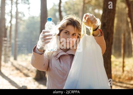 Donna triste, delusa, volontario e assistente pulire la foresta da rifiuti di plastica, rifiuti. Mostra il sacchetto dei rifiuti e il flacone Foto Stock