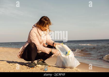 Donna attivista e assistente pulizia spiaggia sabbiosa da rifiuti subacquei, mare o oceano con rifiuti di plastica. Cambiamento globale. Foto Stock