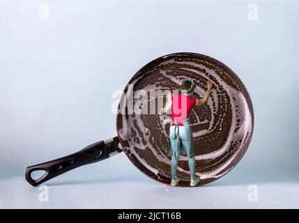 Foto divertente. Una ragazza in un grembiule lava una padella enorme con Foto Stock