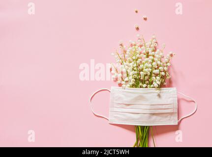 gigli della valle e una maschera medica su sfondo rosa. fiore allergia concetto. Foto Stock