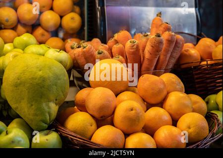 La frutta viene raccolta e impilata sul bancone del mercato per spremere il succo su una pressa manuale. Frutta assortita in un bicchiere trasparente. Foto Stock