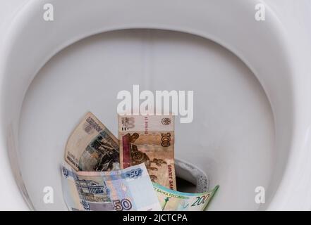 Banconote di rubli russi in primo piano nella tazza bianca del gabinetto. Mettere a fuoco il centro dell'immagine. Vista dall'alto Foto Stock