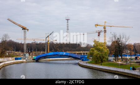 Cantiere di un ponte pedonale e di edifici lungo il fiume Svislach a Minsk Upper City, Bielorussia, con gru da cantiere. Foto Stock