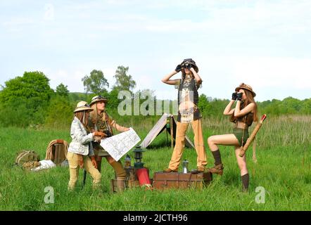 Quattro ragazze sono viste come esploratori. Sono visti al loro campeggio nella natura selvaggia all'aperto. Indossano cappelli safari e abiti cachi. Foto Stock